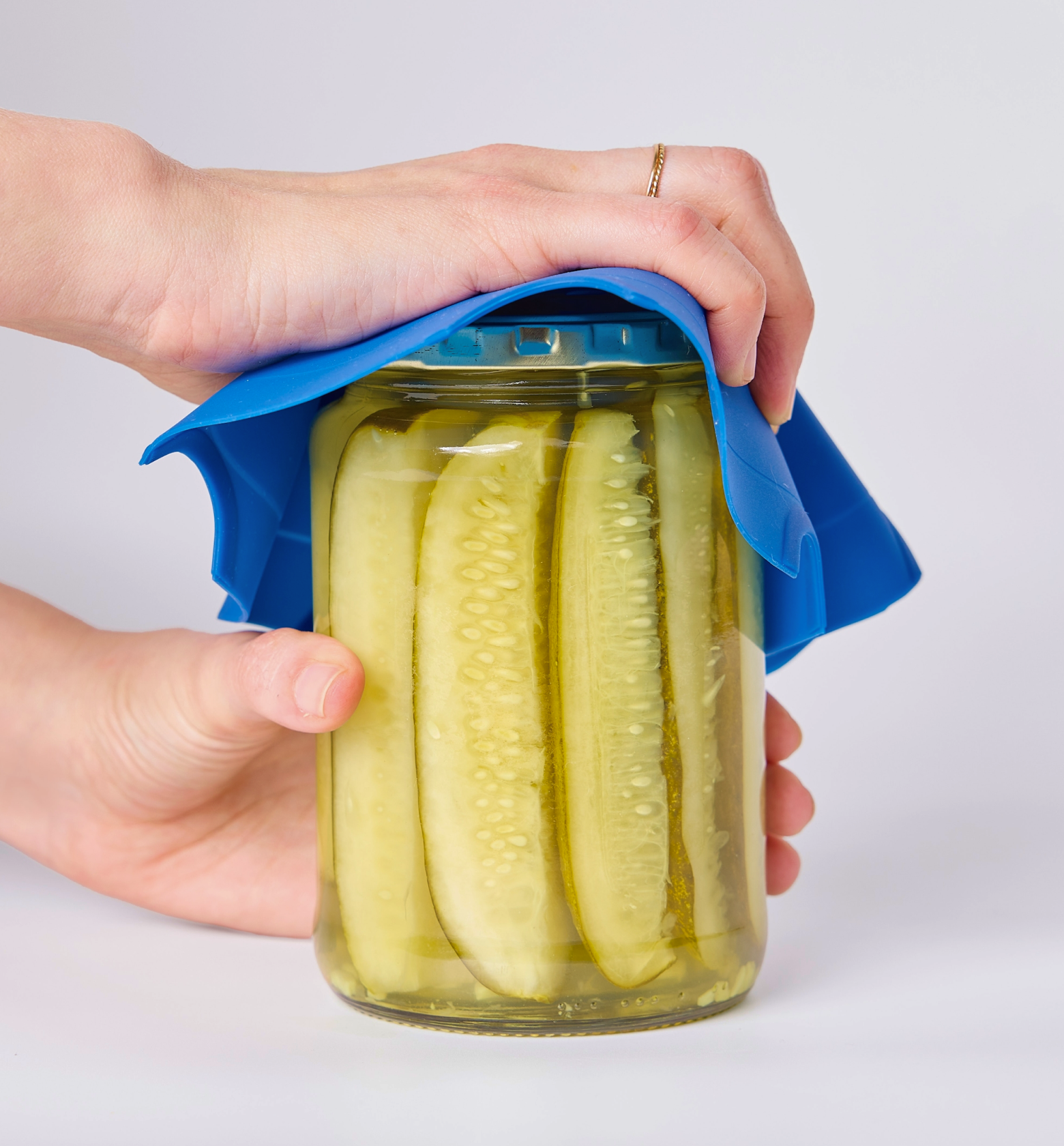 Hands using blue silicone jar opener grip to open a large pickle jar